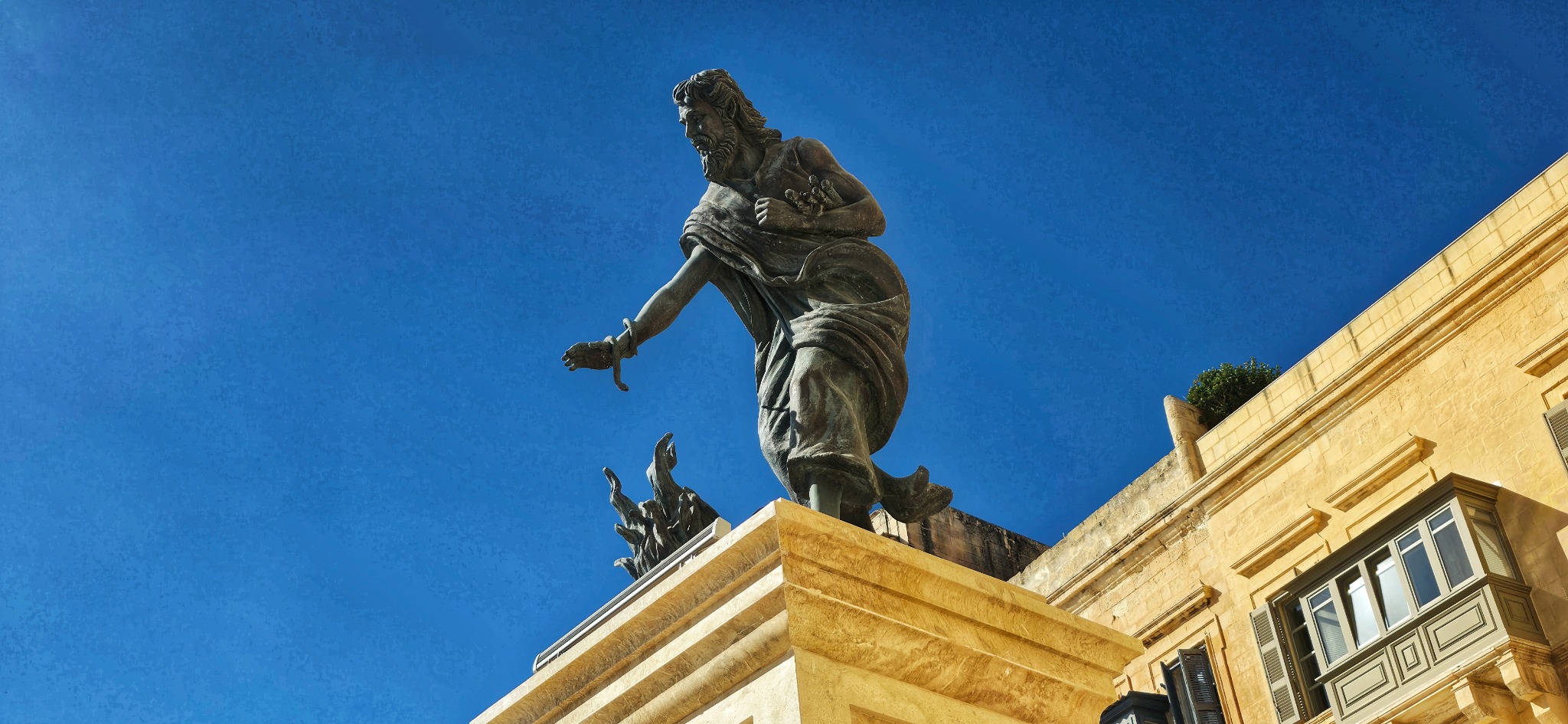 A dramatic bronze sculpture against the blue Valletta sky